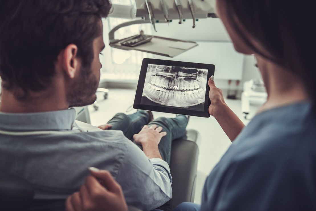 dentista mostrando rdiografía a cliente de espaldas